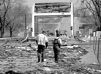Two men walking across debris-strewn bridge in Willmar (black & white photo)