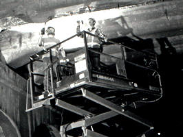 2 men on machine inspecting under a bridge at night