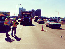 Man, woman in safety vest on bridge with traffic