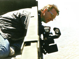 Man & video camera hanging over bridge