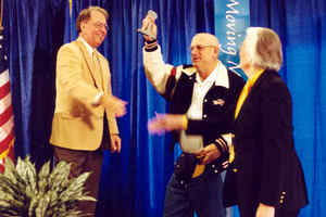 Man holding award, flanked by man, woman