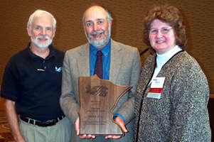 Man holding award, flanked by man, woman