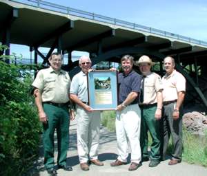 5 men under bridge holding plaque