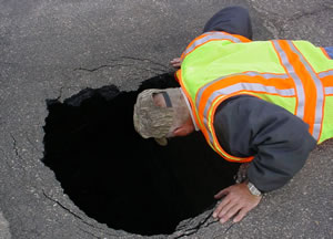 Hwy worker peers into large hole in road