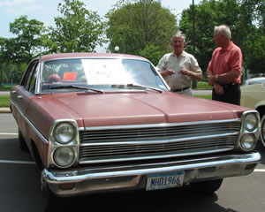 2 men standing next to old hwy car