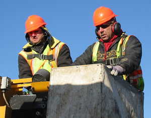 2 men in a bucket above a bridge