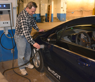 Photo of Tom Tufenk recharging one of MnDOT’s electric vehicle cars.