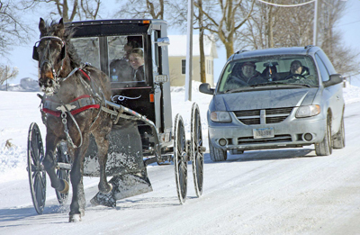 Photo of an Amish buggy with a van behind it.