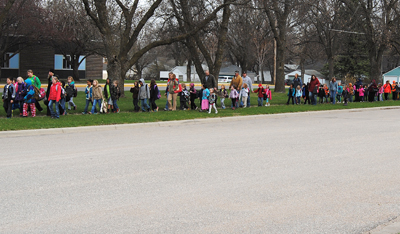 2 dozen kids and adults walking on grass along road