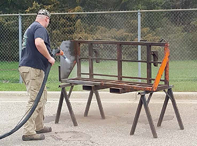 Photo of a man using a vapor blaster to remove paint and rust from a metal object