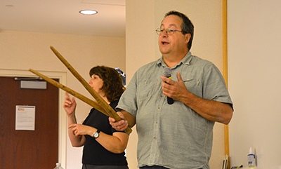 Paul Rice demonstrates use of wood sticks to harvest wild rice. Sign language interpreter is in background.