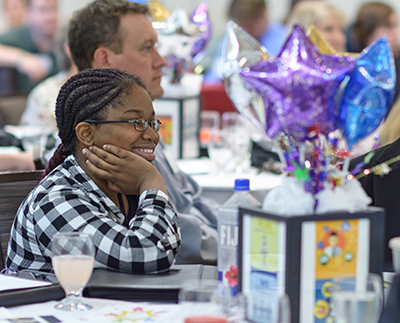 Angel Glass smiles at table while listening to speaker at Seeds and Phoenix Day