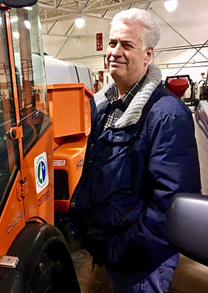 Man in blue jacket standing next to orange MnDOT truck in a truck station