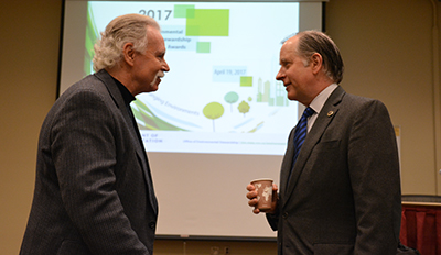 Scott Bradley and Commissioner Zelle talk in front of presentation screen