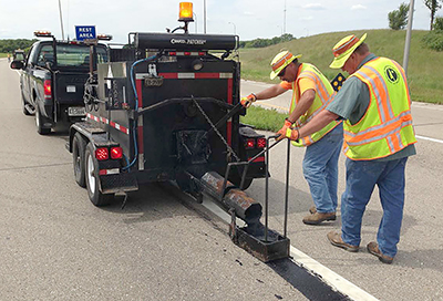 Photo of maintenance workers applying mastic on road cracks.