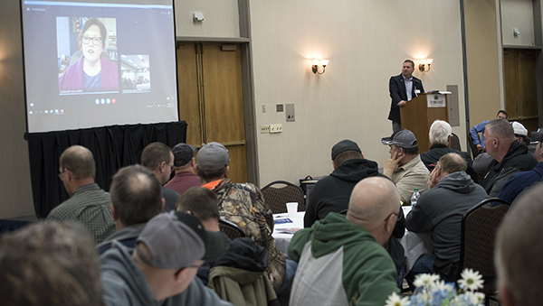 Picture of Margaret Anderson Kelliher, MnDOT commissioner, greeting employees while being projected on a movie screen in a large conference room.