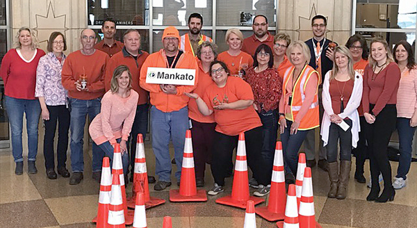 Picture of District 7 employees gathered in their building lobby, wearing orange shirts near road cones.
