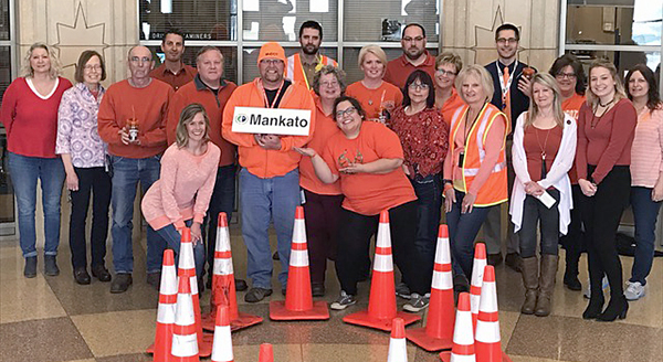Picture of District 7 employees gathered in their building lobby, wearing orange shirts near road cones.