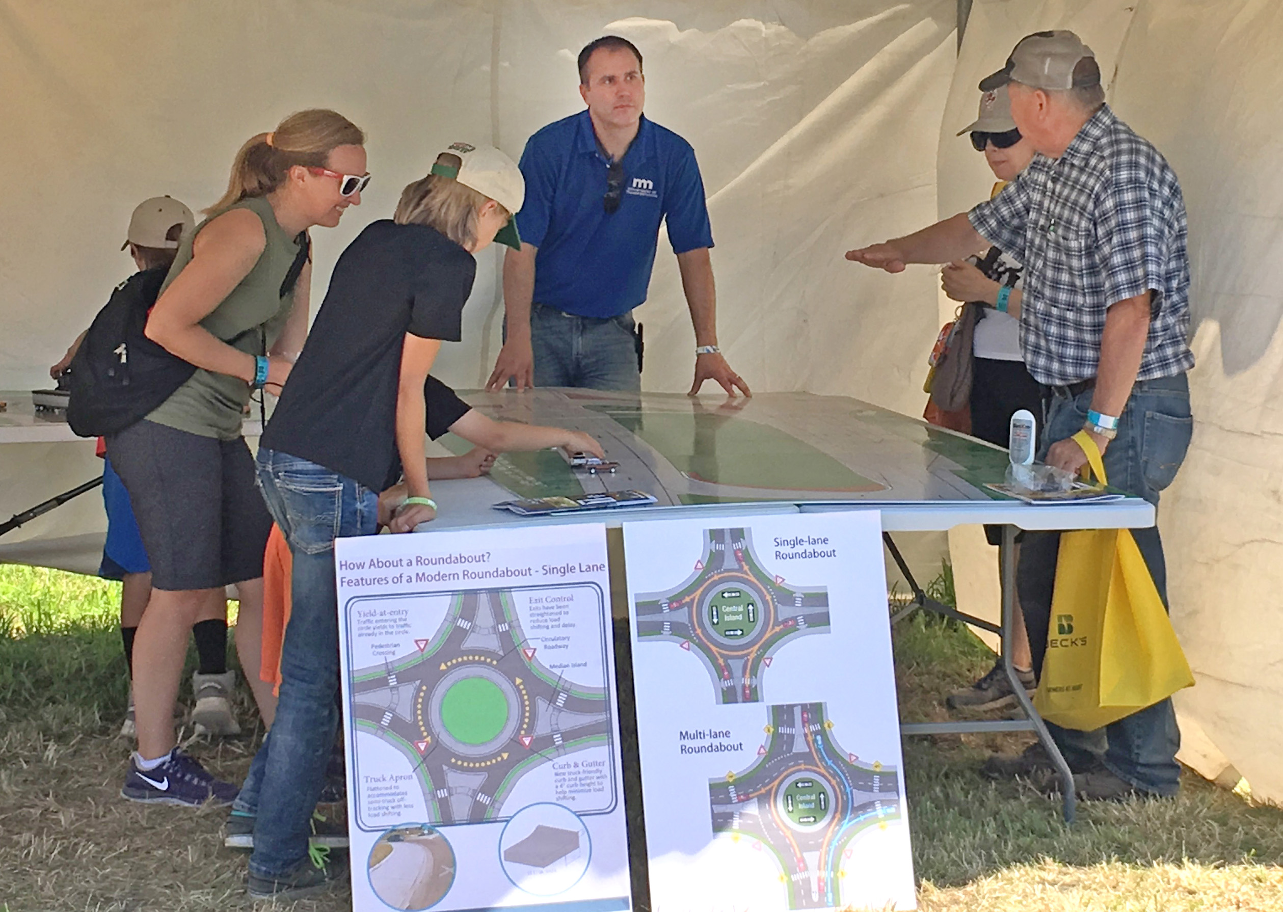 A man in a blue MnDOT shirt listens as a fairgoer points to something on a roundabout map.