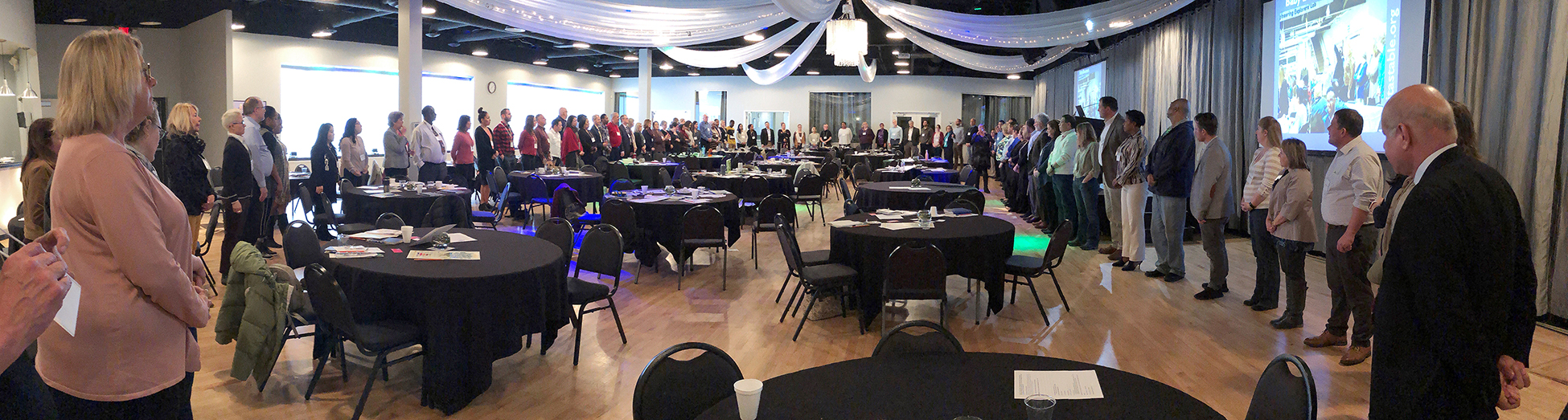 This photo shows people gathered in a large circle around an auditorium with tables