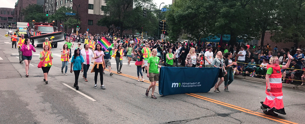 Nearly 20 people walking through downtown Minneapolis. Some are wearing safety vests. The person in the front has a road cone costume on