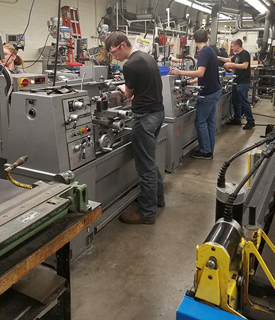 4 students in a metal workshop fabricating parts