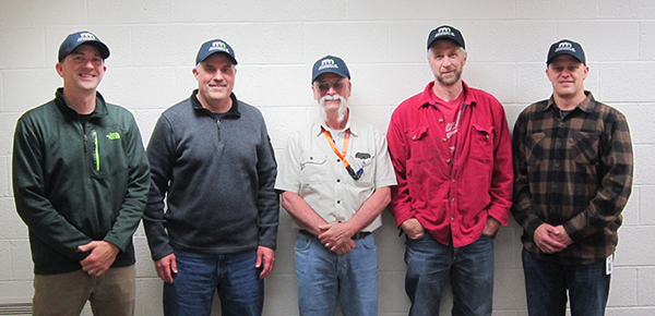 Picture of five men standing against a wall and looking at the camera.