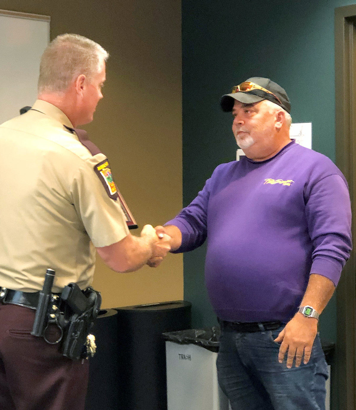 A state trooper and a man in a purple shirt shaking hands