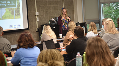 A smiling woman stands in front of a large group in a classroom setting.