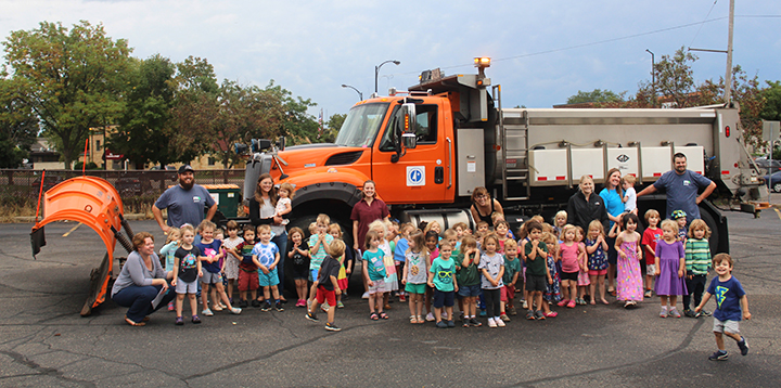 A group of small children are lined up in front of a large MnDOT snowplow truck