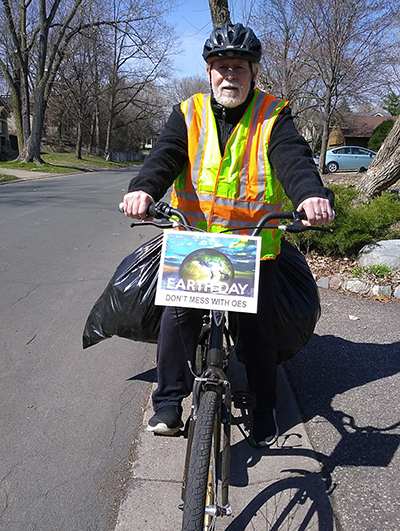 Photo: a man on a bike, with a large bacg full of trash slung over the back of it