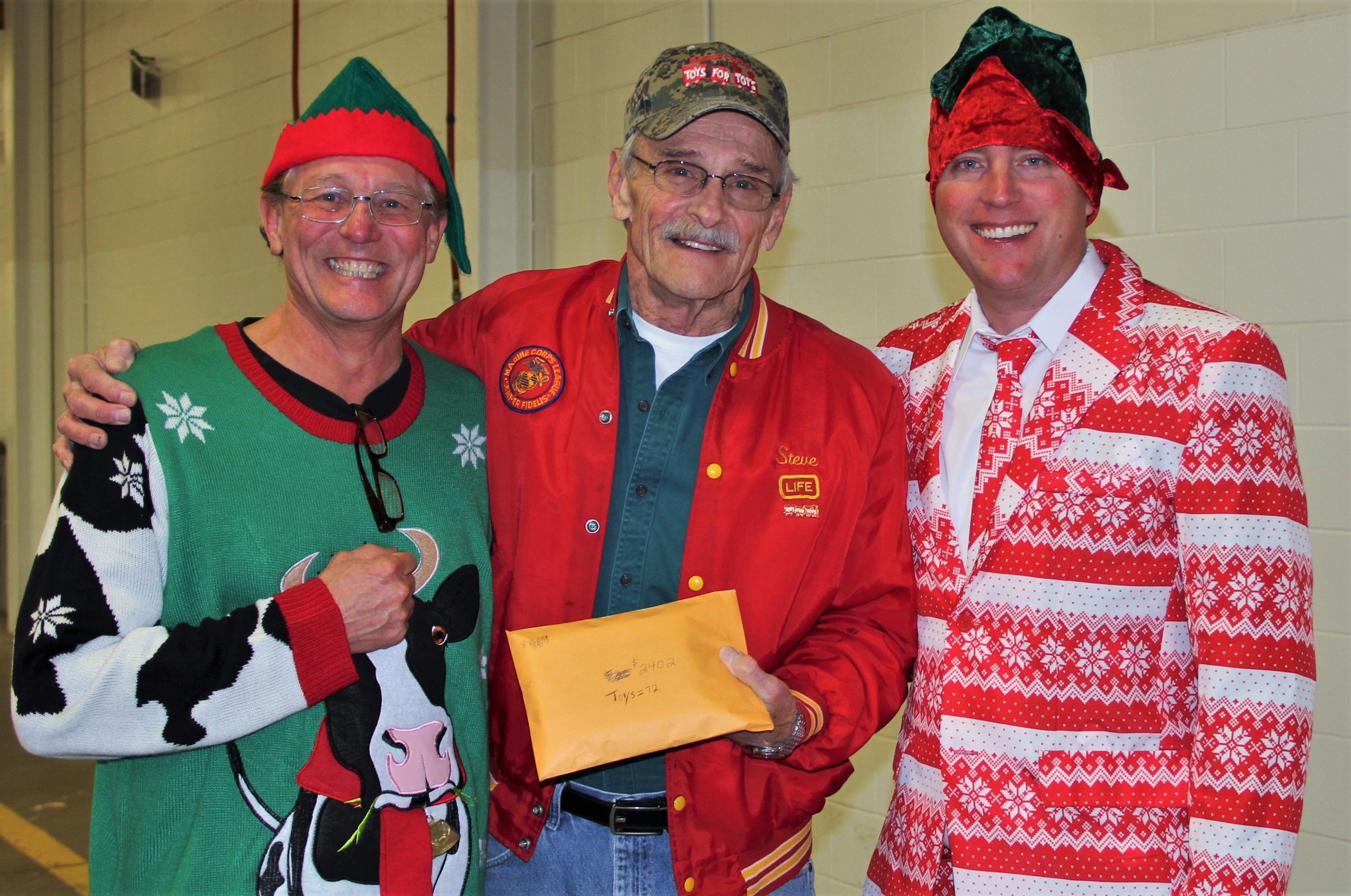 Photo: three men posing together, with the middle one holding a donation envelope