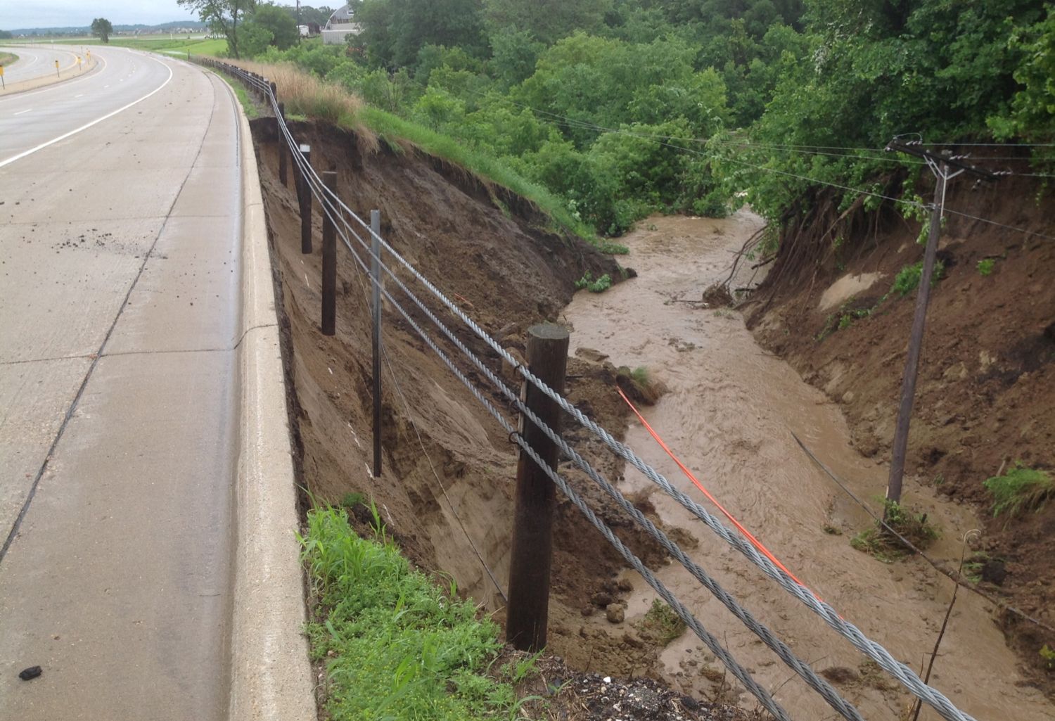 Photo: a torrent of brown water rushes past a stretch of paved road.