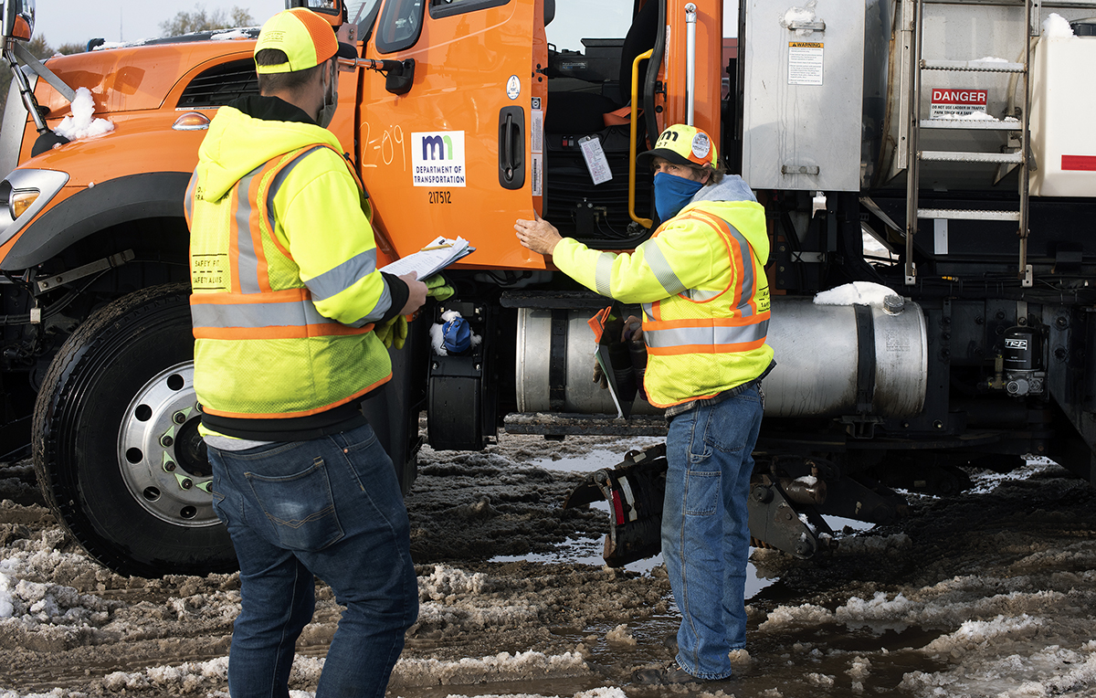 Photo: two MnDOT employees, masked, near a snowplow during training