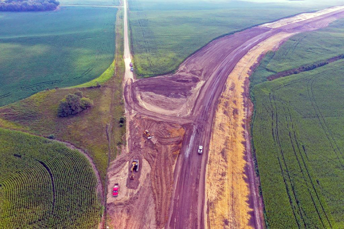 Photo: an aerial shot of a road being built, with planted crops on either side
