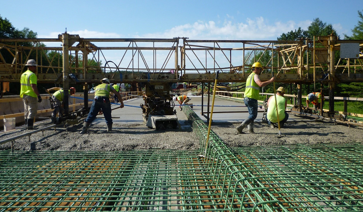 Bridge crew smooths concrete between green steel bars on bridge deck