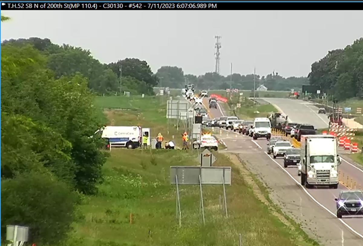 Traffic camera shot of several figures clustered around a motorcycle at the side of the road