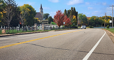 Photo of a road in front of a church and cemetary.