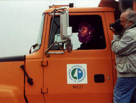 Woman driving truck with cameraman on runninboard