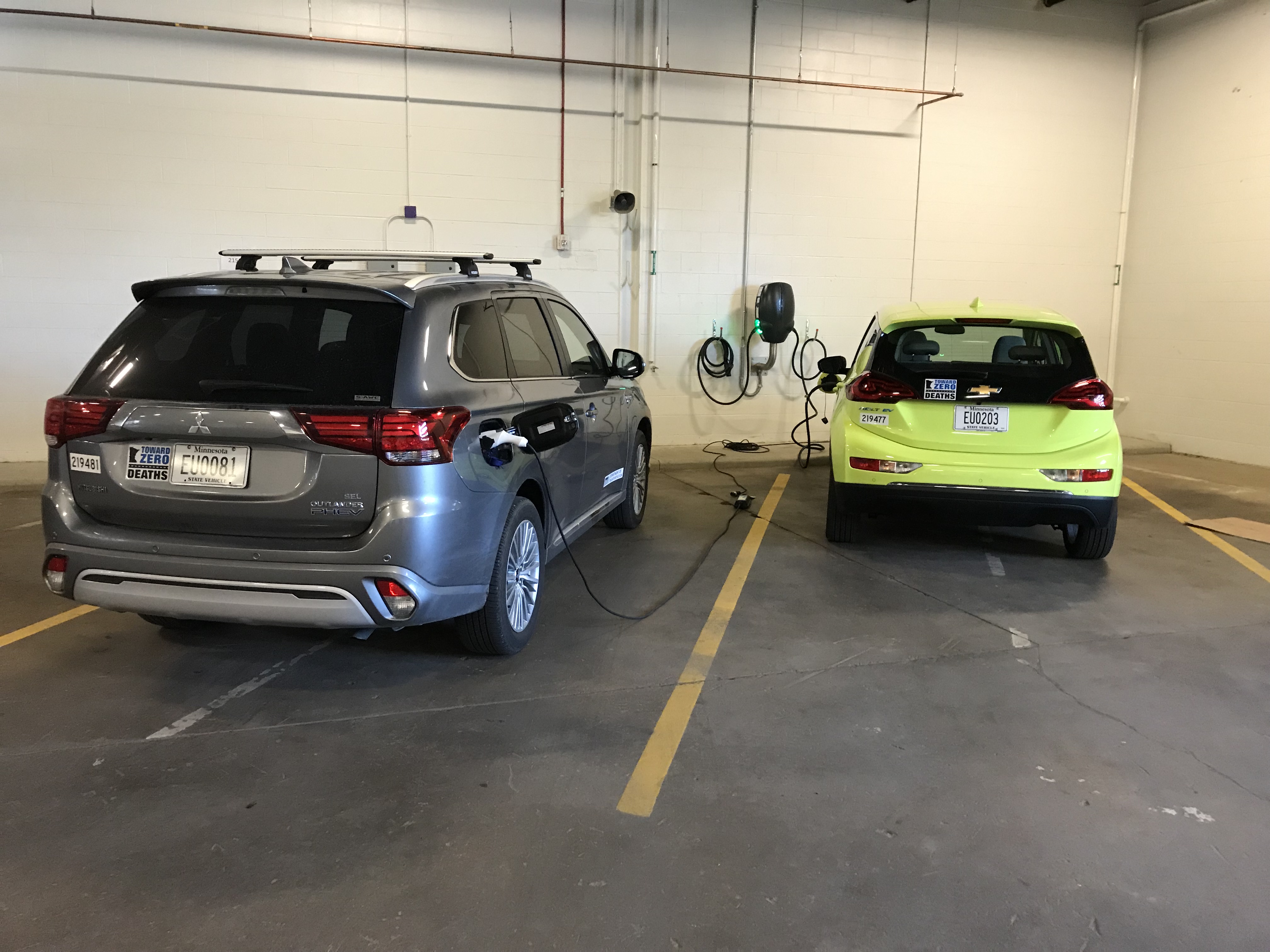 Two cars parked in a garage, with both plugged into a wall mounted charger
