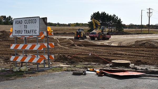 A sign marked road closed to thru traffic sits near an empty stretch of dirt where the road will be