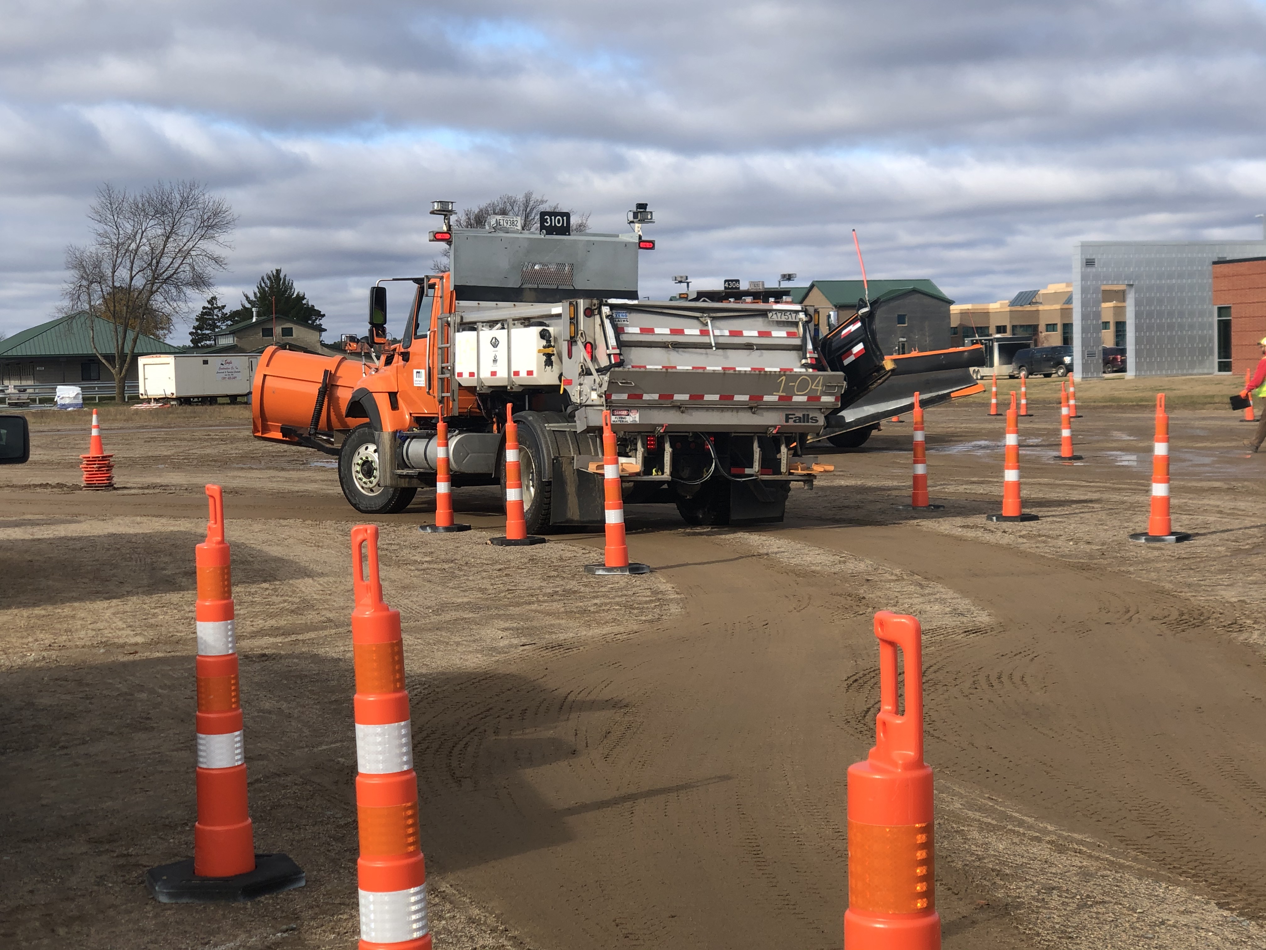 An orange MnDOT plow truck makes its way down a dirt path lined with cones.