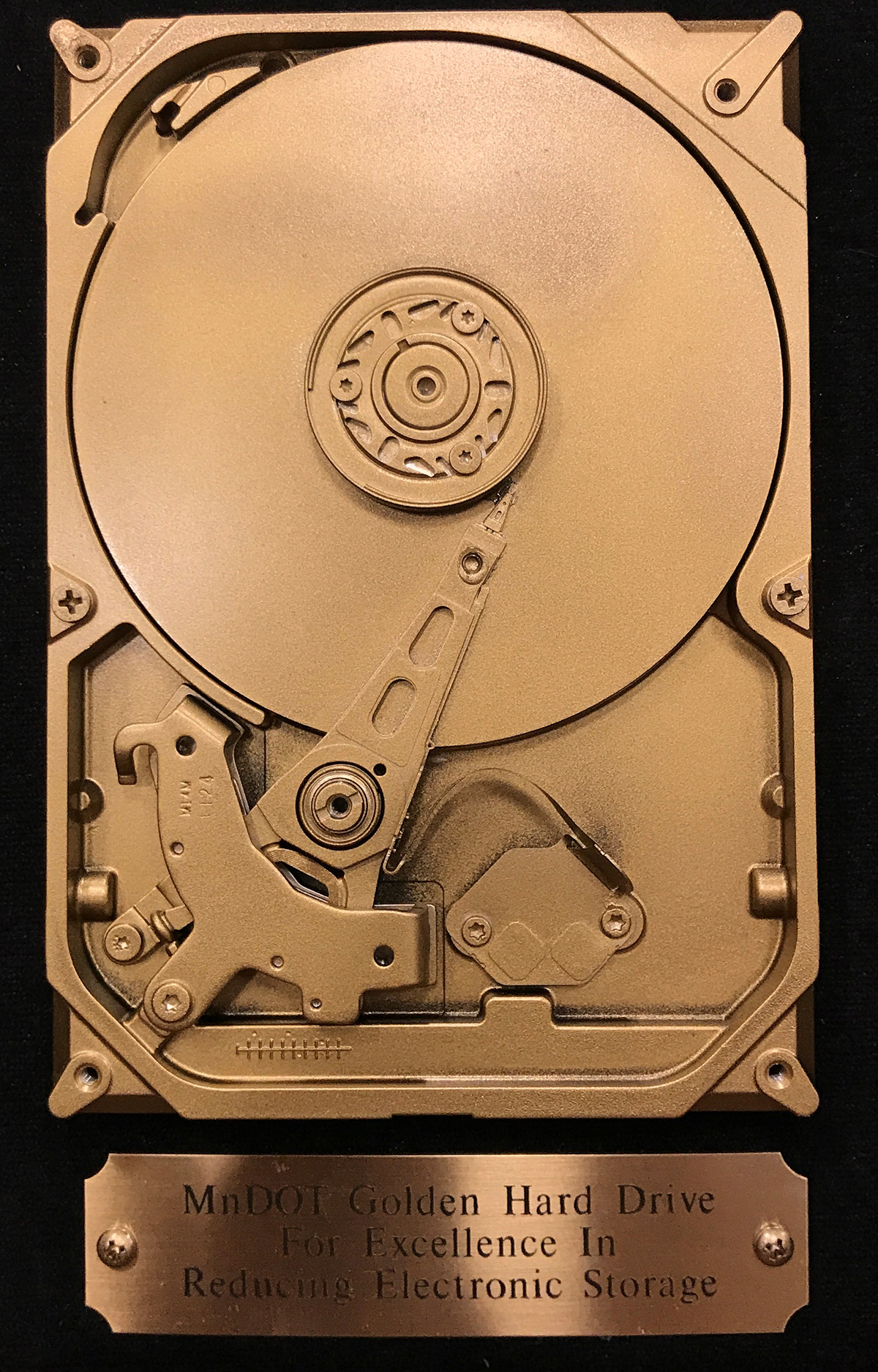 Photo: the golden hard drive award is an old computer hard drive painted gold. A brass plate underneath this hard drive says MnDOT golden hard drive for excellence in reduced electronic storage