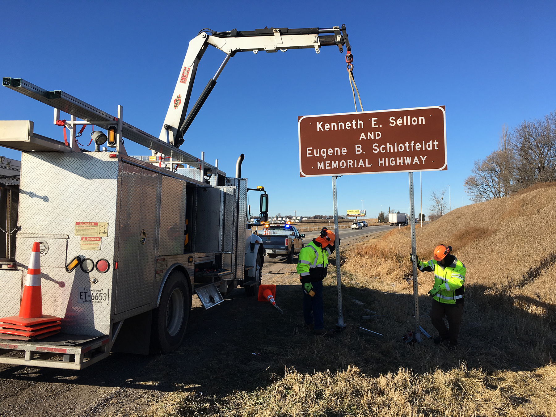 Photo: work crews install a sign on the side of Interstate 94. The sign says Kenneth E Sellon and Eugene B Schlotfeldt memorial highway