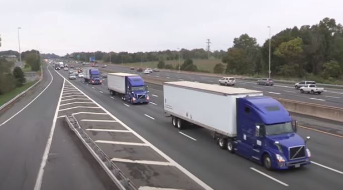 Photo: three purple semi trucks travelling in a single line on a highway