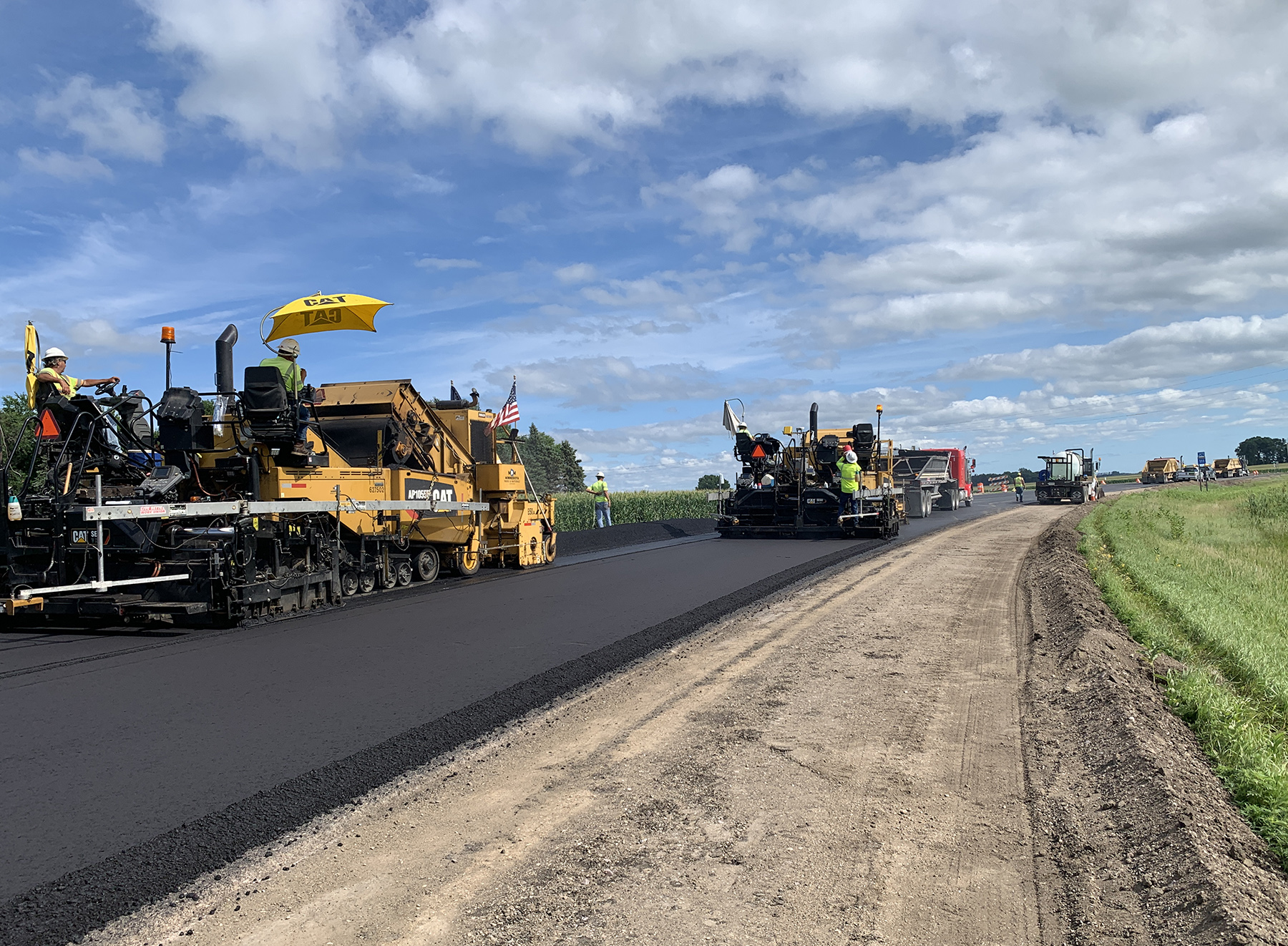 Photo: two paving machines move side-by-side down a freshly paved road