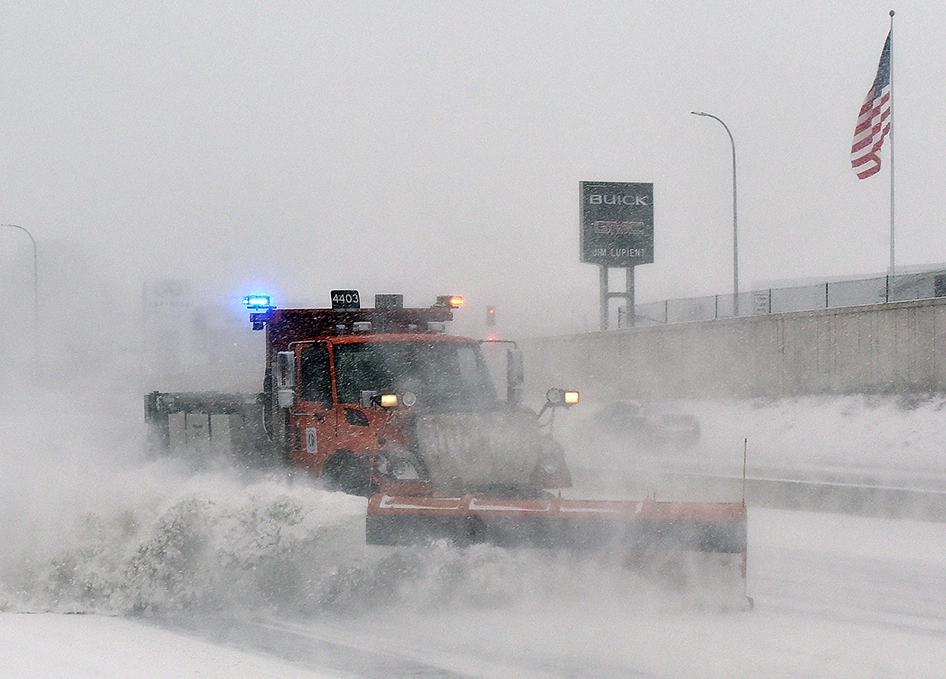 Photo: a snowplow kicks up a wake of snow while plowing on the highway