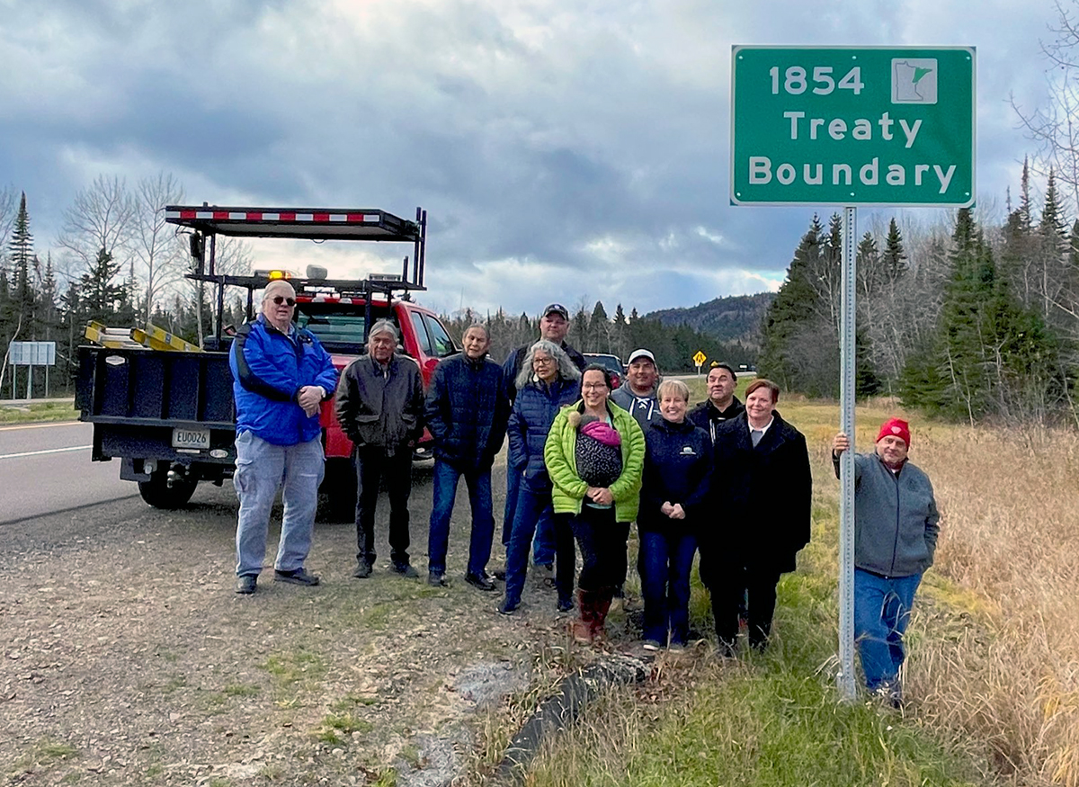 A group of people standing near a sign, which reads 1854 treaty boundary